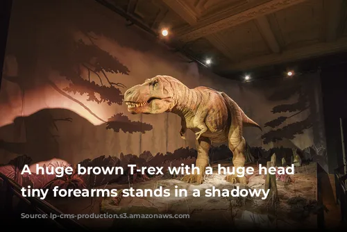 A huge brown T-rex with a huge head and tiny forearms stands in a shadowy space