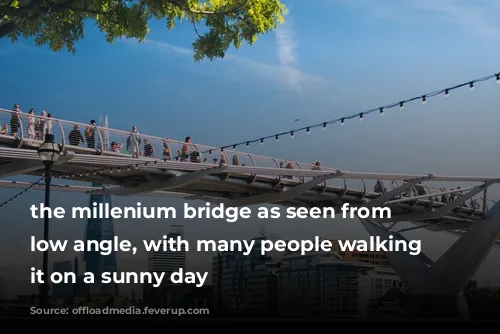 the millenium bridge as seen from a low angle, with many people walking across it on a sunny day