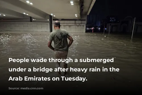 People wade through a submerged street under a bridge after heavy rain in the United Arab Emirates on Tuesday.