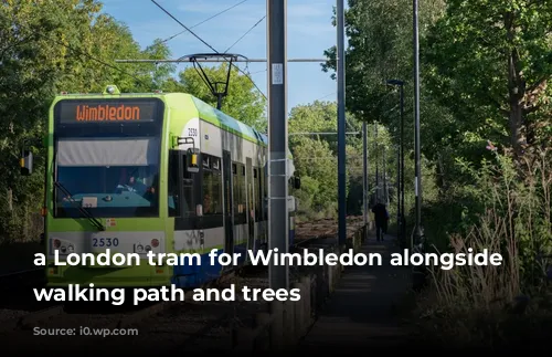 a London tram for Wimbledon alongside a walking path and trees