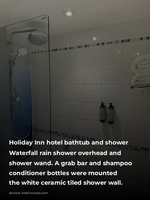 Holiday Inn hotel bathtub and shower combination. Waterfall rain shower overhead and handheld shower wand. A grab bar and shampoo and conditioner bottles were mounted on the white ceramic tiled shower wall. 