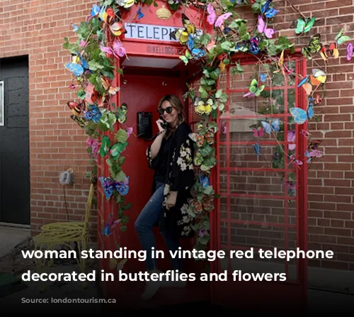 woman standing in vintage red telephone booth decorated in butterflies and flowers 