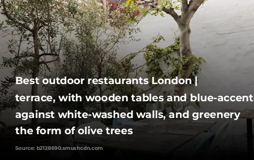 Best outdoor restaurants London | Mazi's terrace, with wooden tables and blue-accented furniture against white-washed walls, and greenery in the form of olive trees