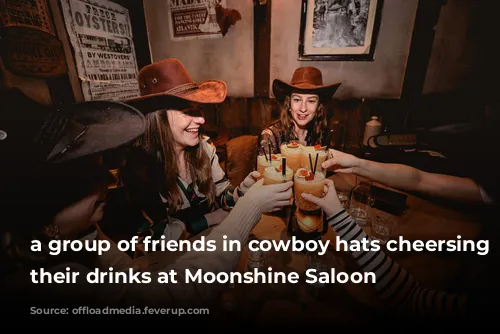 a group of friends in cowboy hats cheersing with their drinks at Moonshine Saloon