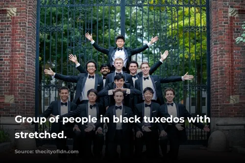 Group of people in black tuxedos with arms stretched.