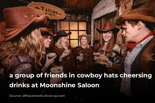 a group of friends in cowboy hats cheersing their drinks at Moonshine Saloon