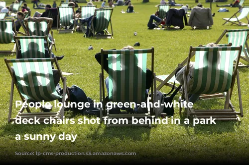 People lounge in green-and-white striped deck chairs shot from behind in a park on a sunny day