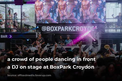 a crowd of people dancing in front of a DJ on stage at BoxPark Croydon