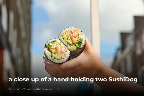 a close up of a hand holding two SushiDog rolls