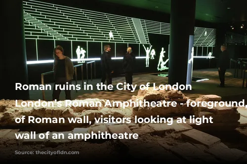 Roman ruins in the City of London - London’s Roman Amphitheatre - foreground, section of Roman wall, visitors looking at light up wall of an amphitheatre 